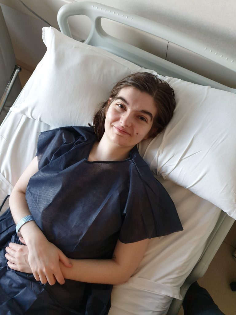 A photo of Charlie, a woman before surgery in a hospital bed and surgical gown.