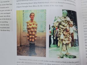 Photograph of artistic references in a book. There are two images on the page, one is of the artist Louise Bourgeois from a performance as Artemis, 1980. The other image is of Betsy Damon in a street performance as 'The 7,000-year-old-woman, 1977.