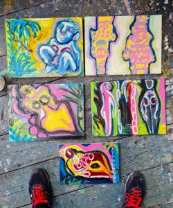Photograph of my studio floor, and 5 colourful rectangular paintings of female figures in nature.