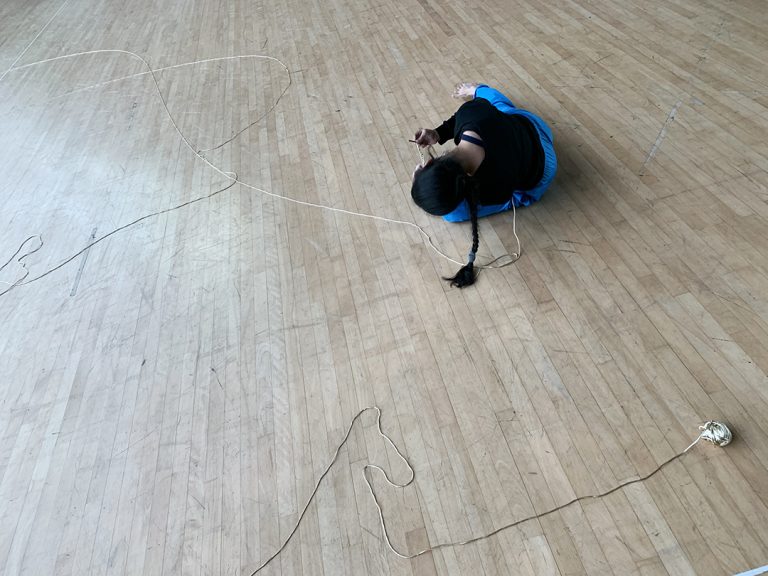 Asian woman in black top and blue pants doing body movement on the floor with a white yarn - closer shot