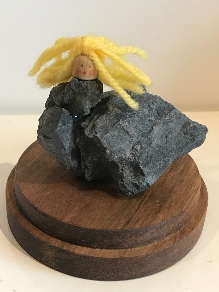A girl hybrid sculpture - the head of a blonde girl model, attached to a group of dark grey rocks that have been glued together to form the girl's abstract body