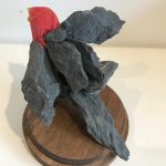 A bird hybrid sculpture - the head of a lifelike red bird model, attached to a group of dark grey rocks that have been glued together to form the bird’s body - two wings flapped out, a body and a tail.