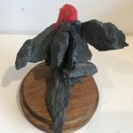 A bird hybrid sculpture - the head of a lifelike red bird model, attached to a group of dark grey rocks that have been glued together to form the bird’s body - two wings flapped out, a body and a tail.