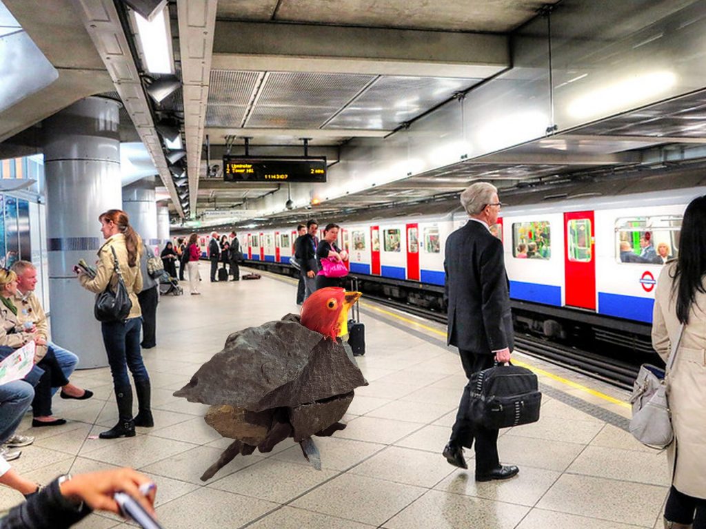 A bird hybrid - the head of a lifelike red bird model, attached to a group of dark grey rocks that have been glued together to form the bird’s body - two wings flapped out, a body and a tail. The image of the sculpure is being used a part of a collage in a digital photo of the subway scene