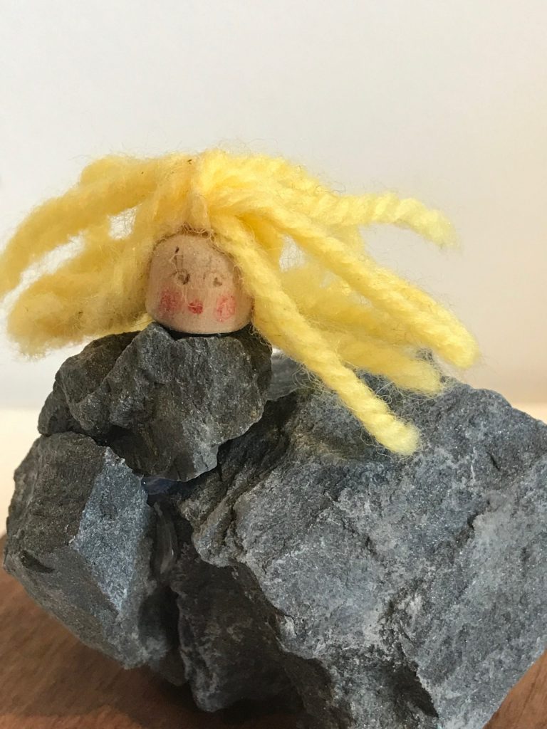 A girl hybrid sculpture - the head of a blonde girl model, attached to a group of dark grey rocks that have been glued together to form the girl's abstract body