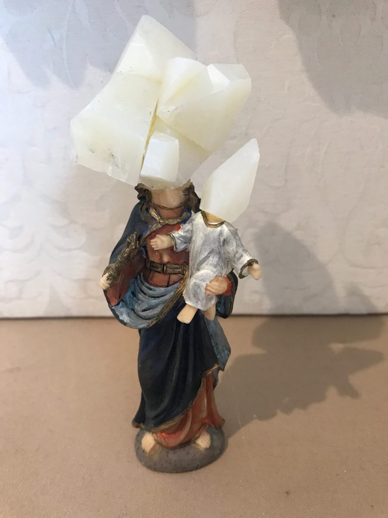 Zoomed out - sculpture of pieces of soap glued together as the head of a saint figurine. Saint is holding a baby whose head is made of soap.