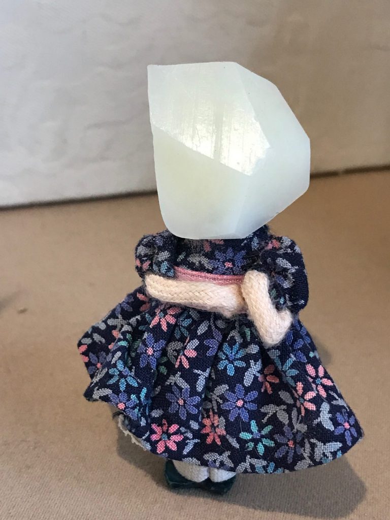 Sculpture of a piece of soap glued as the head of a girl in a blue floral dress figurine.