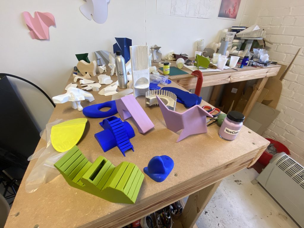 An L shaped workbench with green, blue and lilac playground like sculptures in the foreground