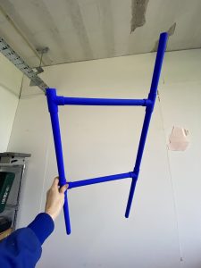 Constructed cobalt blue pipes in a ladder like formation held up against a white wall
