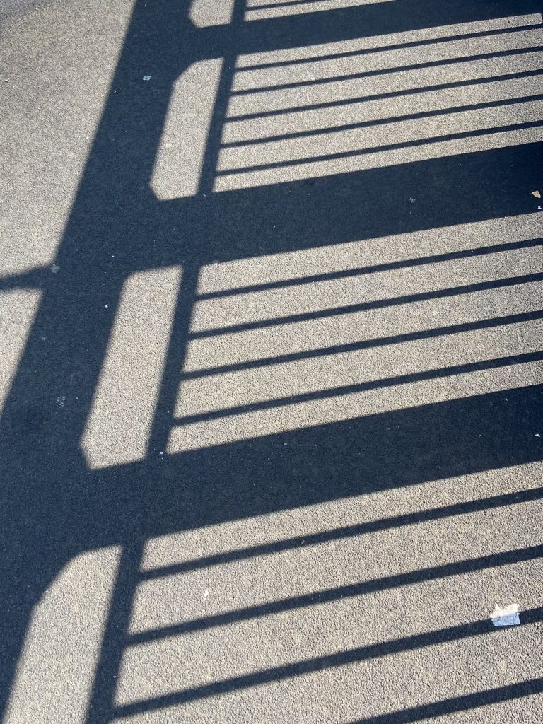 The shadow of bridge railings against the tarmac ground