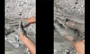 Still from a video depicting two frames side next to each other against a black background. The frames depict hands covered in grey mud.