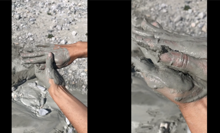 Still from a video depicting two frames side next to each other against a black background. The frames depict hands covered in grey mud.