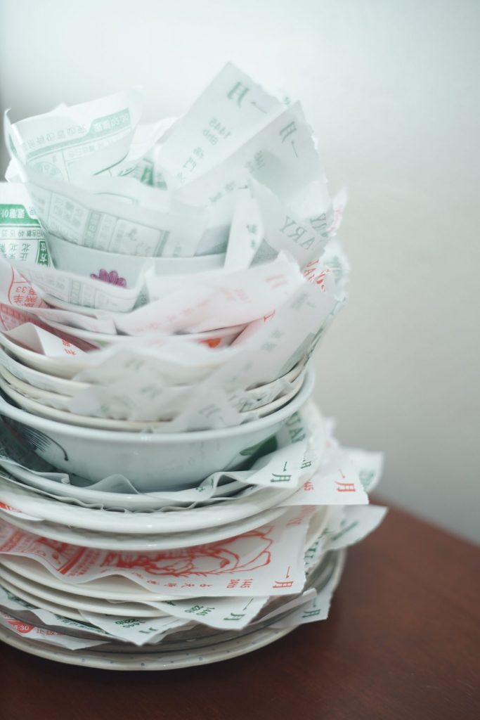 On a wooden table, china plates and bowls of various sizes are stacked on top one another, in between are layered with traditional lunar calendar